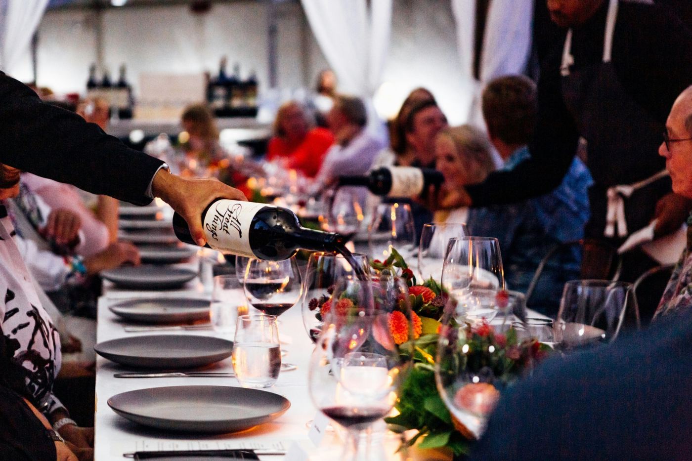Wine being poured along a long, candlelit dinner table